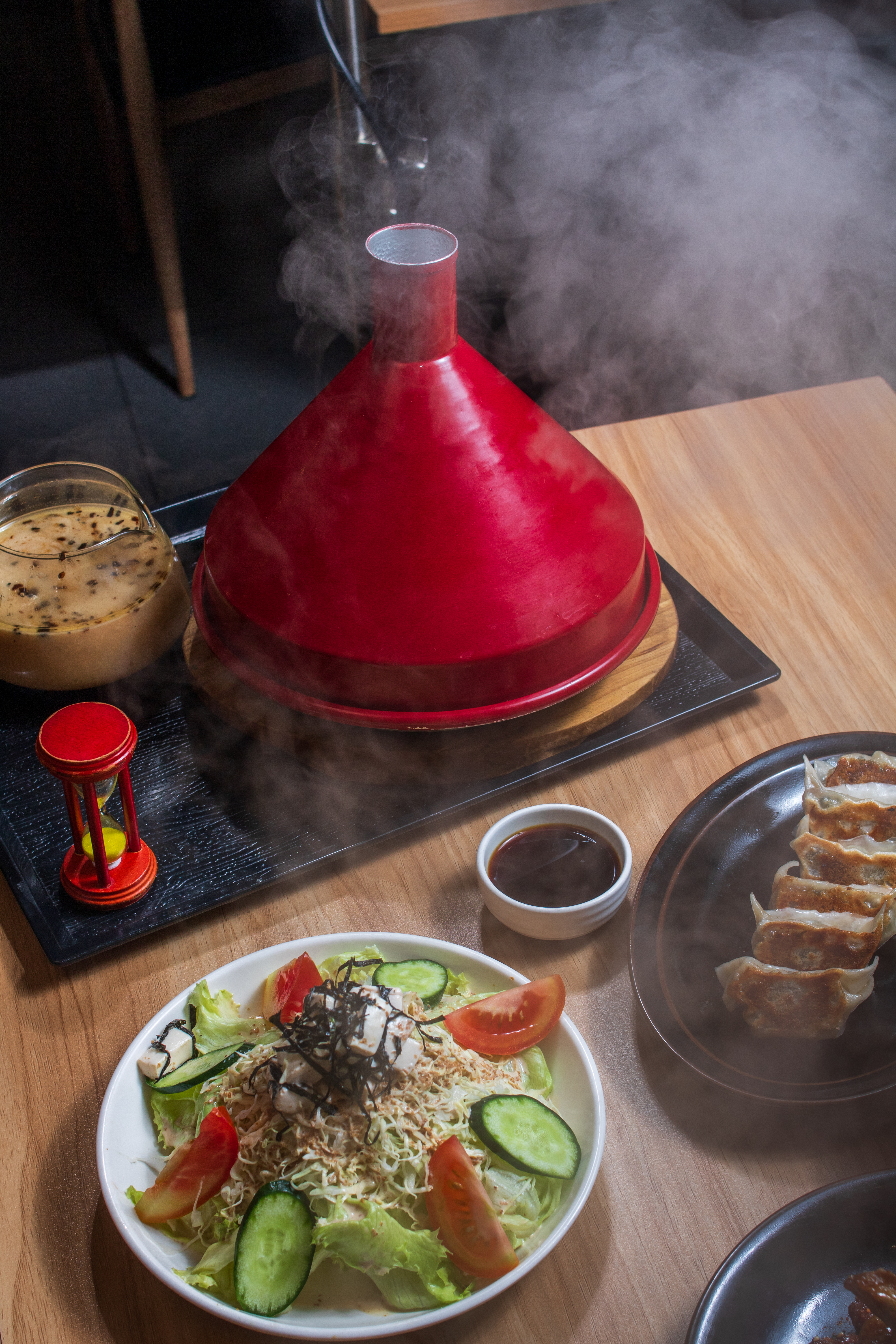 A red Kazan stone steamer releasing steam over a table of dishes